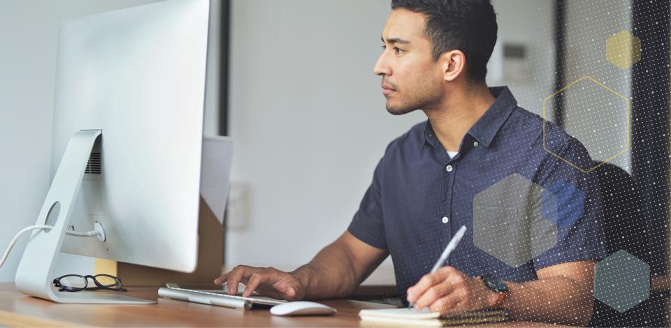 Male employee in front of a computer, taking notes and engaging with content on screen.