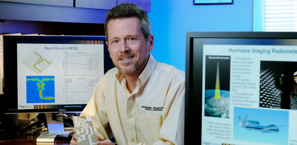 Glenn Hopkins next to computer screens displaying research