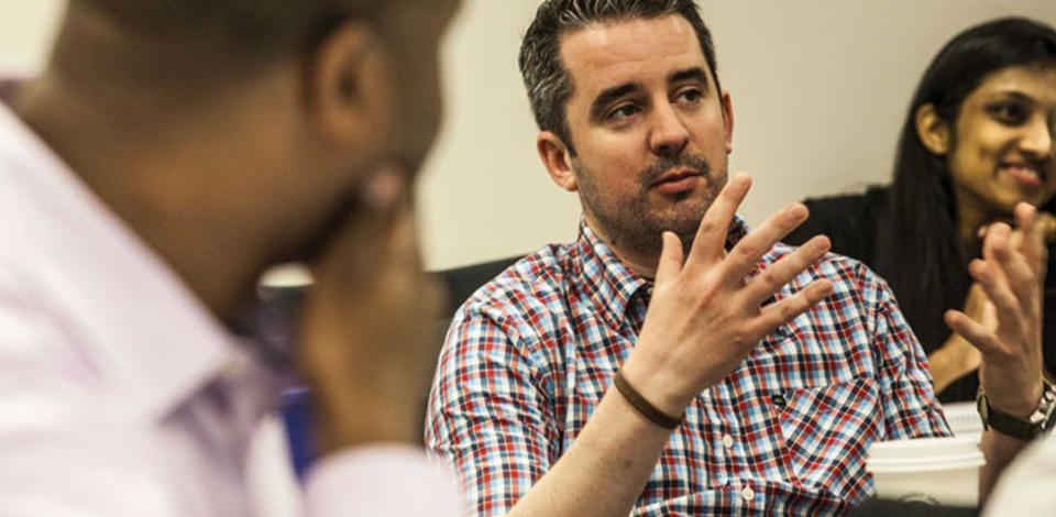 Male learner talking with hands to peers who are intently looking at him