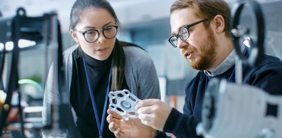 Male and female engineers discussing prototype build with 3D printer.