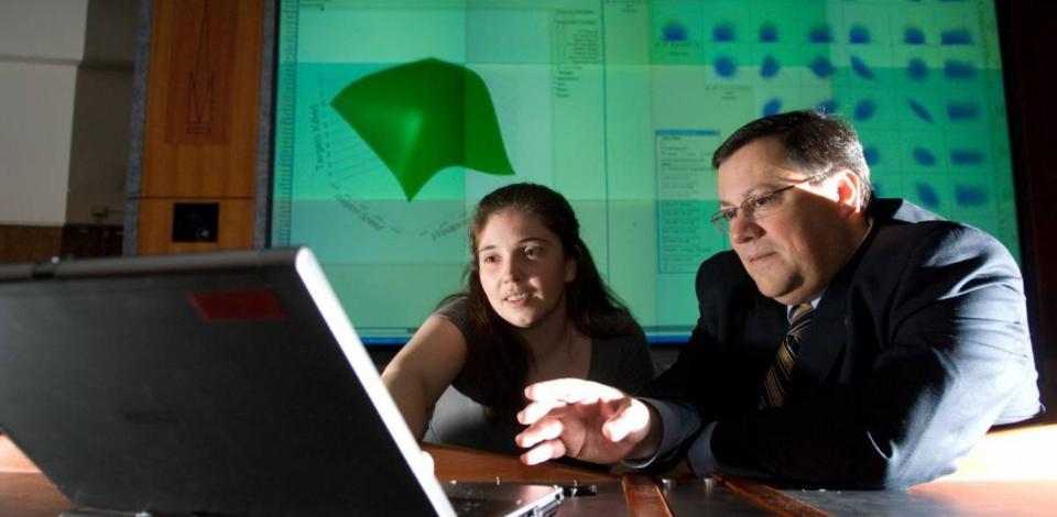 Dimitri Marvis and a female student sitting at a desk in a classroom, looking at a laptop screen.